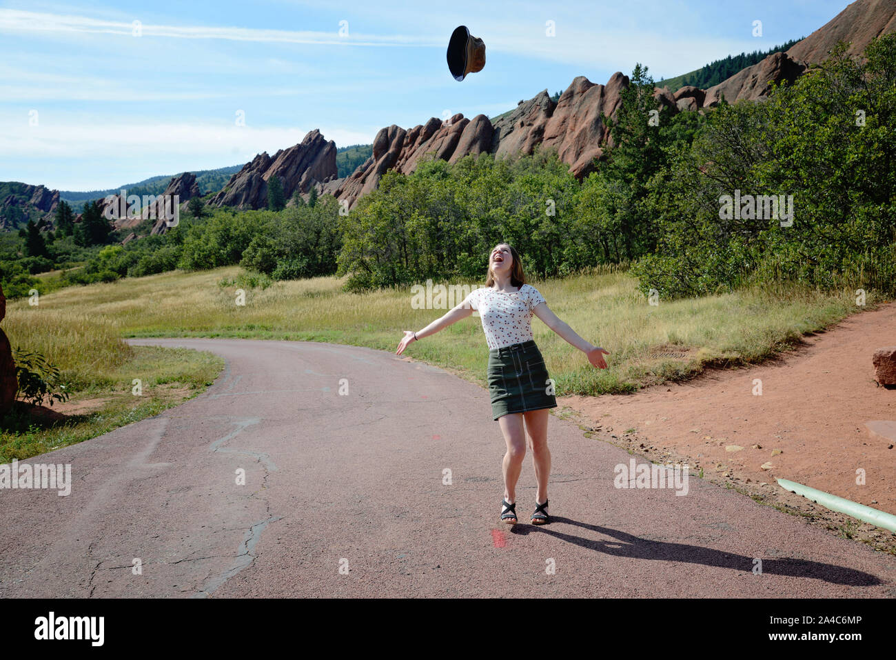 girl throwing hat up in celebration and joy with rocky outcroppings in the background Stock Photo