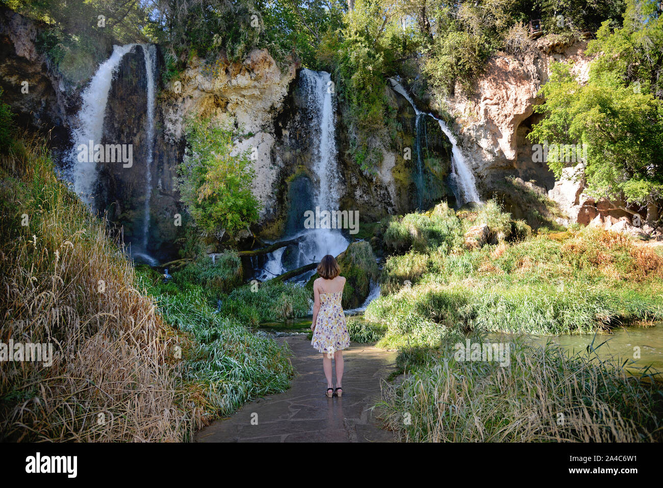 teenage girl in dress standing and looking up at triple waterfall Stock Photo