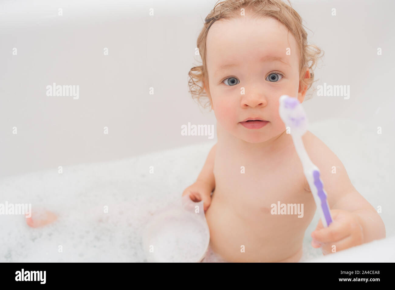 Funny happy baby with curly hair taking bath and brushing her teeth. A
