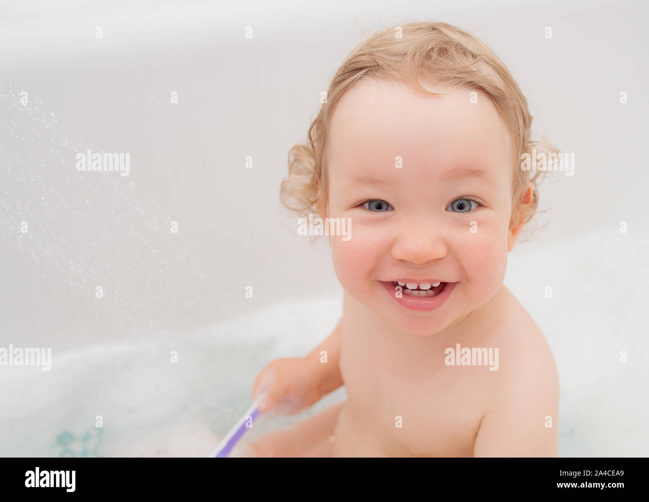 Funny happy baby with curly hair taking bath and brushing her teeth. A