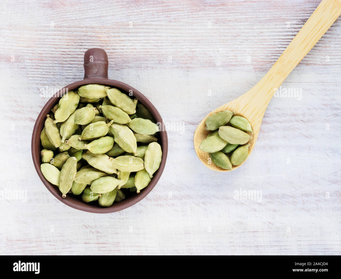 Spice Green cardamom (Elettaria cardamomum) in a clay cup with a spoon on a brown wooden background Stock Photo