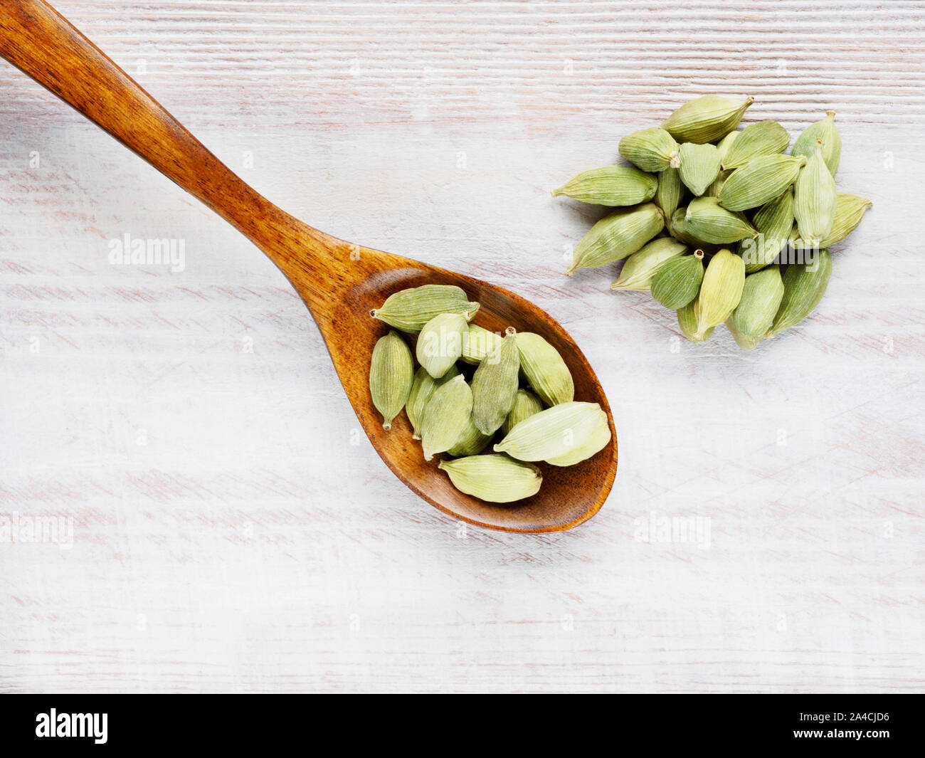 Spice Green cardamom (Elettaria cardamomum) in a spoon diagonally on a brown wooden background Stock Photo