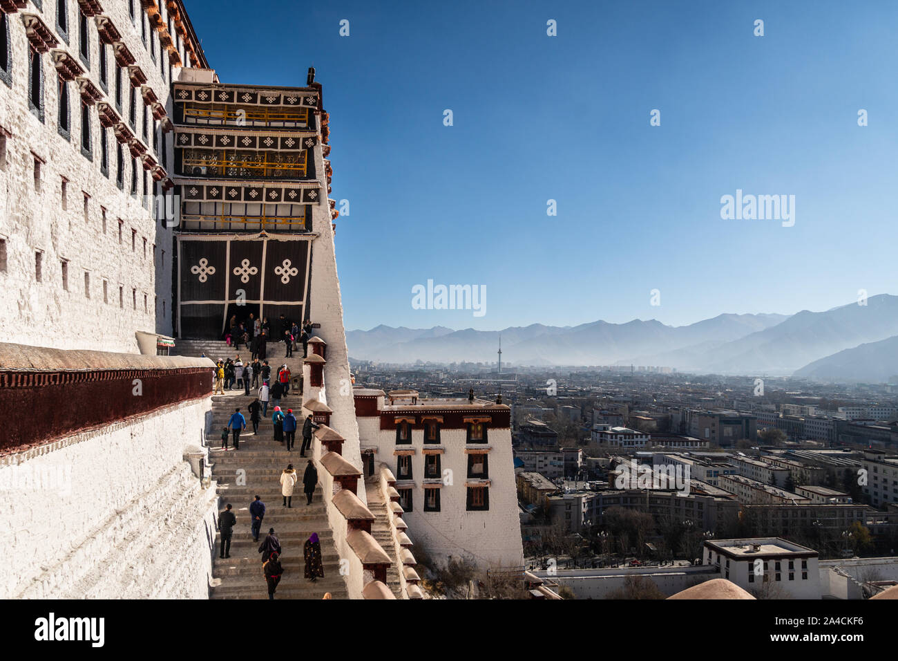 Lhasa, China - December 13 2018: Tourists walk up the stairs leading to the famous Potala Palace in Lhasa old town in Tibet province with the city in Stock Photo