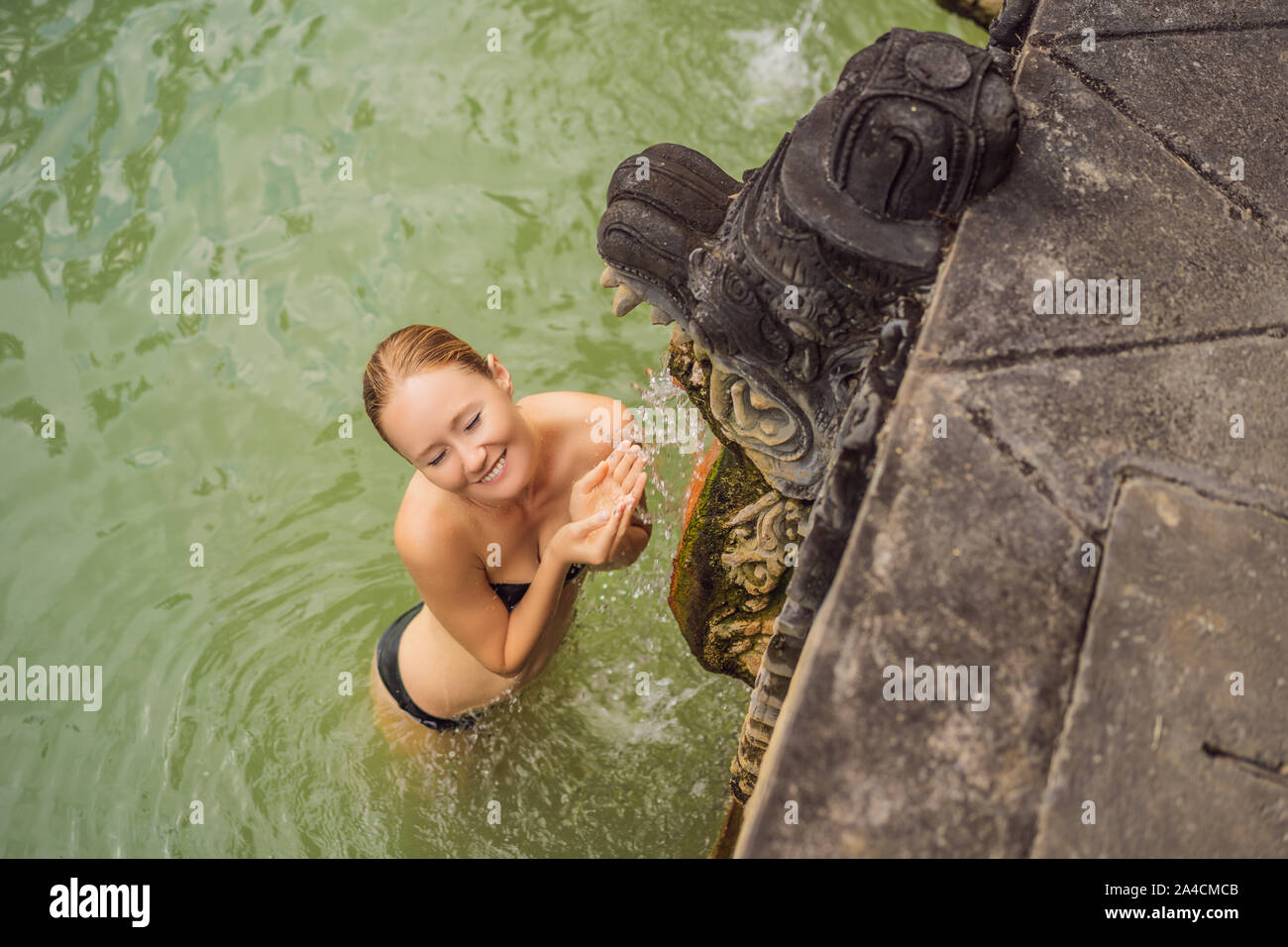 Young woman in hot springs banjar. Thermal water is released from the mouth of statues at a hot springs in Banjar, Bali, Indonesia Stock Photo