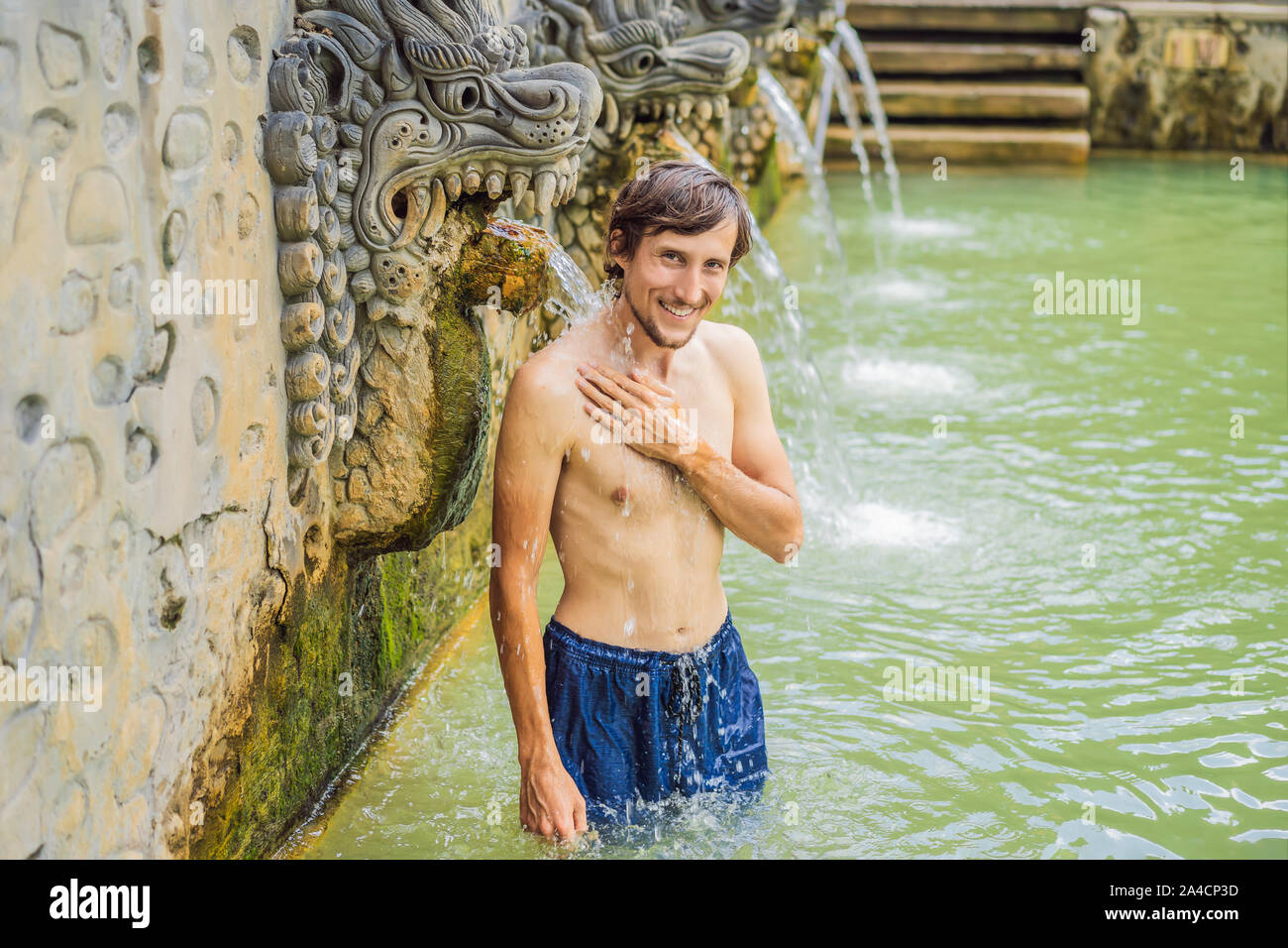 Young man in hot springs banjar. Thermal water is released from the mouth of statues at a hot springs in Banjar, Bali, Indonesia Stock Photo