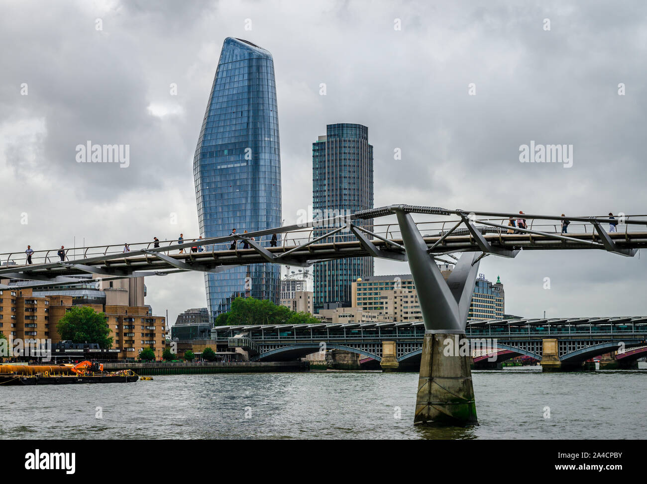 People walk on the Millennium Bridge that spans river Thames, in London. One Blackfriars Tower (aka The Vase) & South Bank Tower are in the background Stock Photo