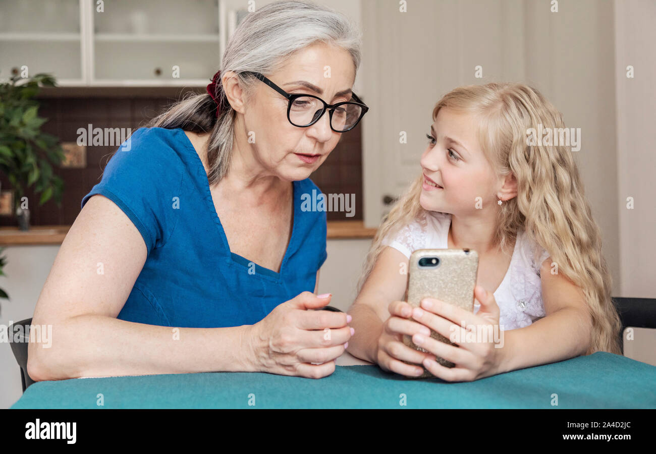 Preschool female kid teaching her grandmother some smartphone tips and tricks Stock Photo