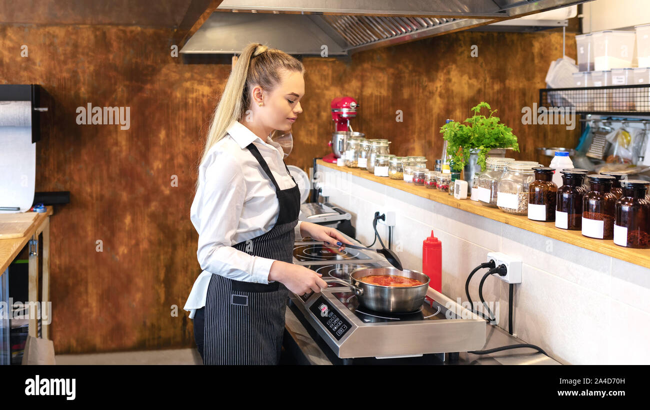 Female chef in restaurant kitchen cooking delicious food on modern electric  stove Stock Photo - Alamy