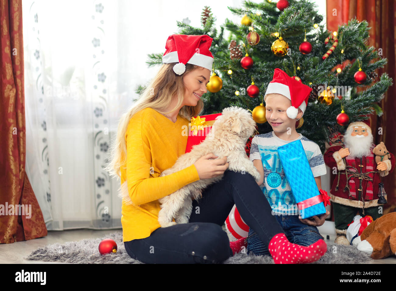 Cheerful single mom and adopted kid celebrating Christmas together with their dog under Christmas tree Stock Photo