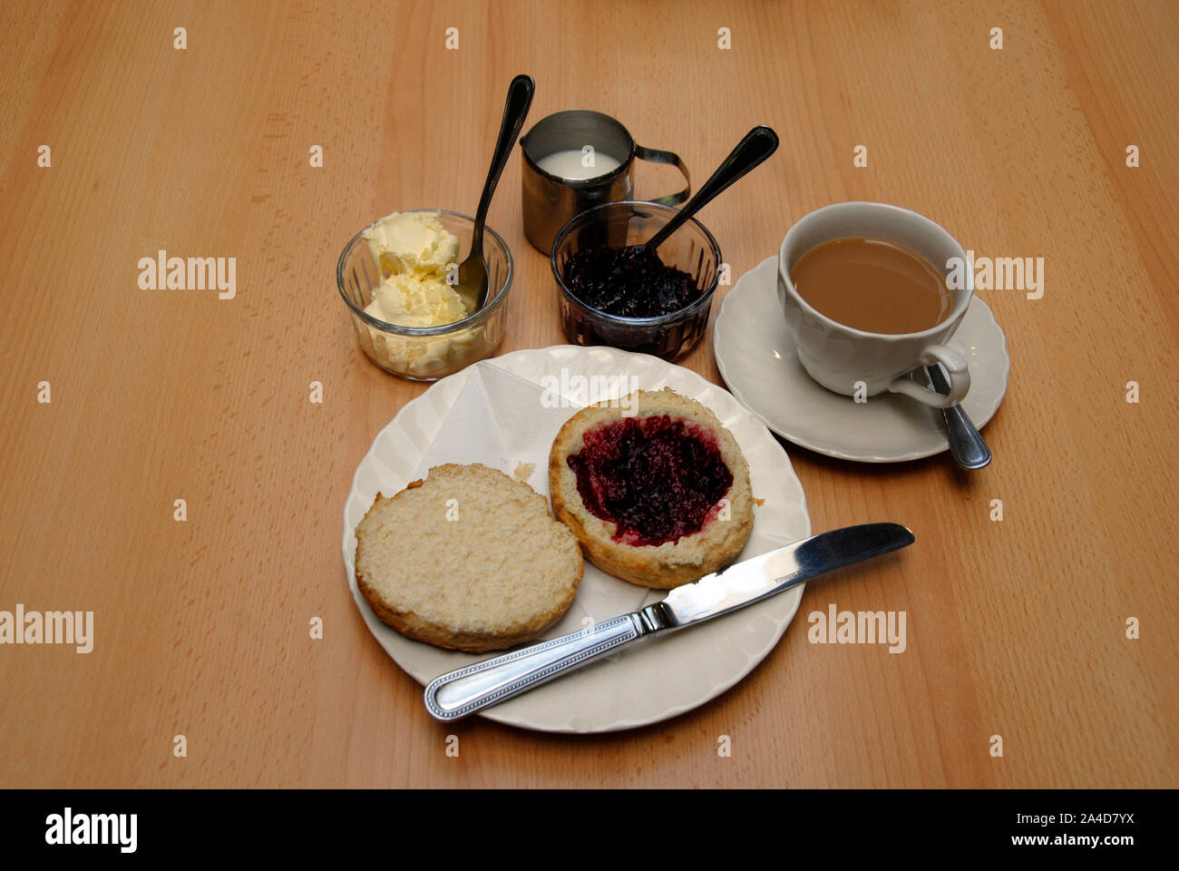 Traditional cream tea with large scone cut in two, with raspberry jam on one half Stock Photo