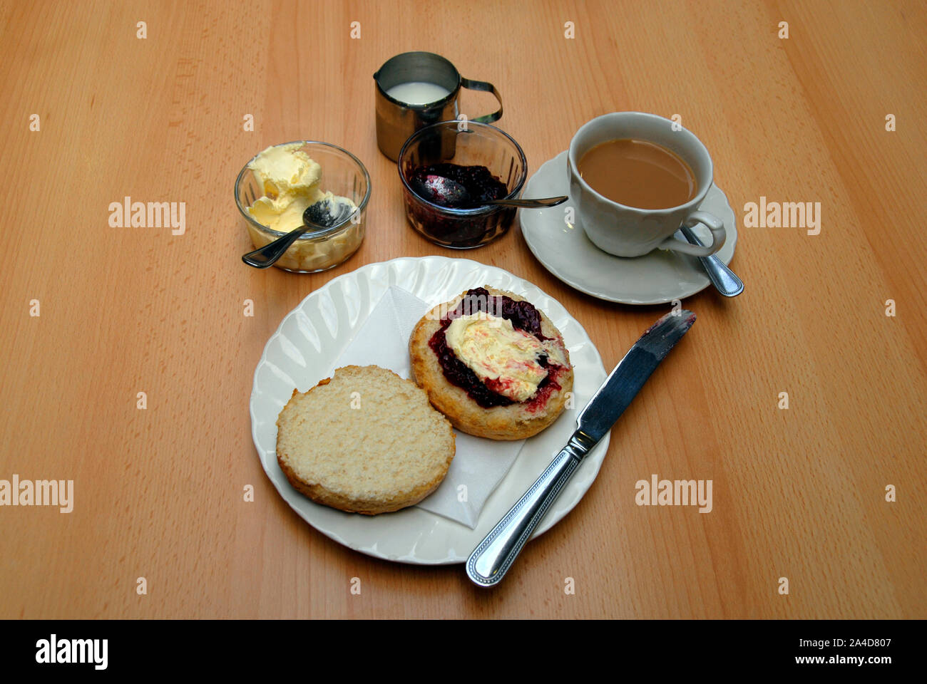 Traditional cream tea with large scone cut in two, with raspberry jam and clotted cream on one half Stock Photo