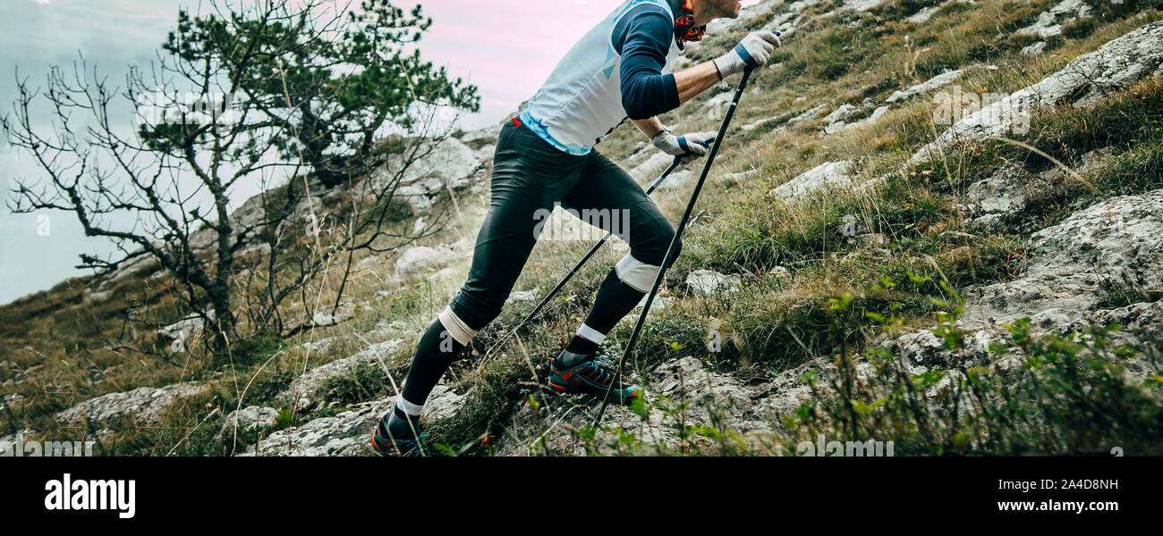 man runner with trekking poles climbing uphill mountain marathon