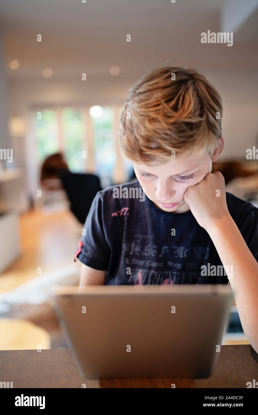 Boy sitting at table using a digital tablet Stock Photo