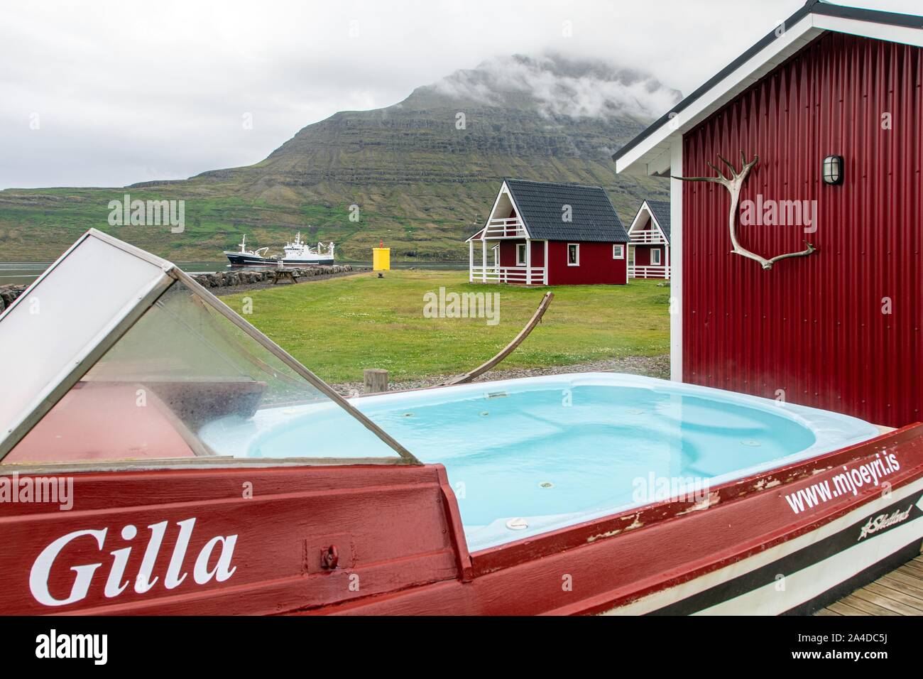 JACUZZI IN FRONT OF THE LITTLE RED HOUSES OF THE CHARMING HOTEL FEROABJONUSTAN MJOEYRI ON THE BANKS OF THE FJORD, ESKIFJORDUR, ICELAND, EUROPE Stock Photo