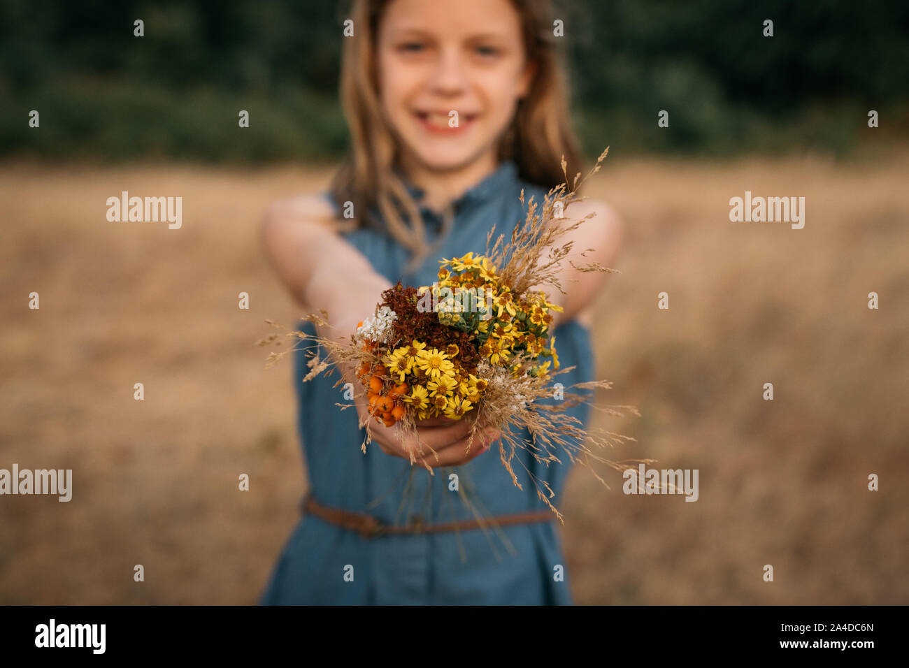 Smiling Girl standing in a field holding a bunch of wildflowers, Netherlands Stock Photo