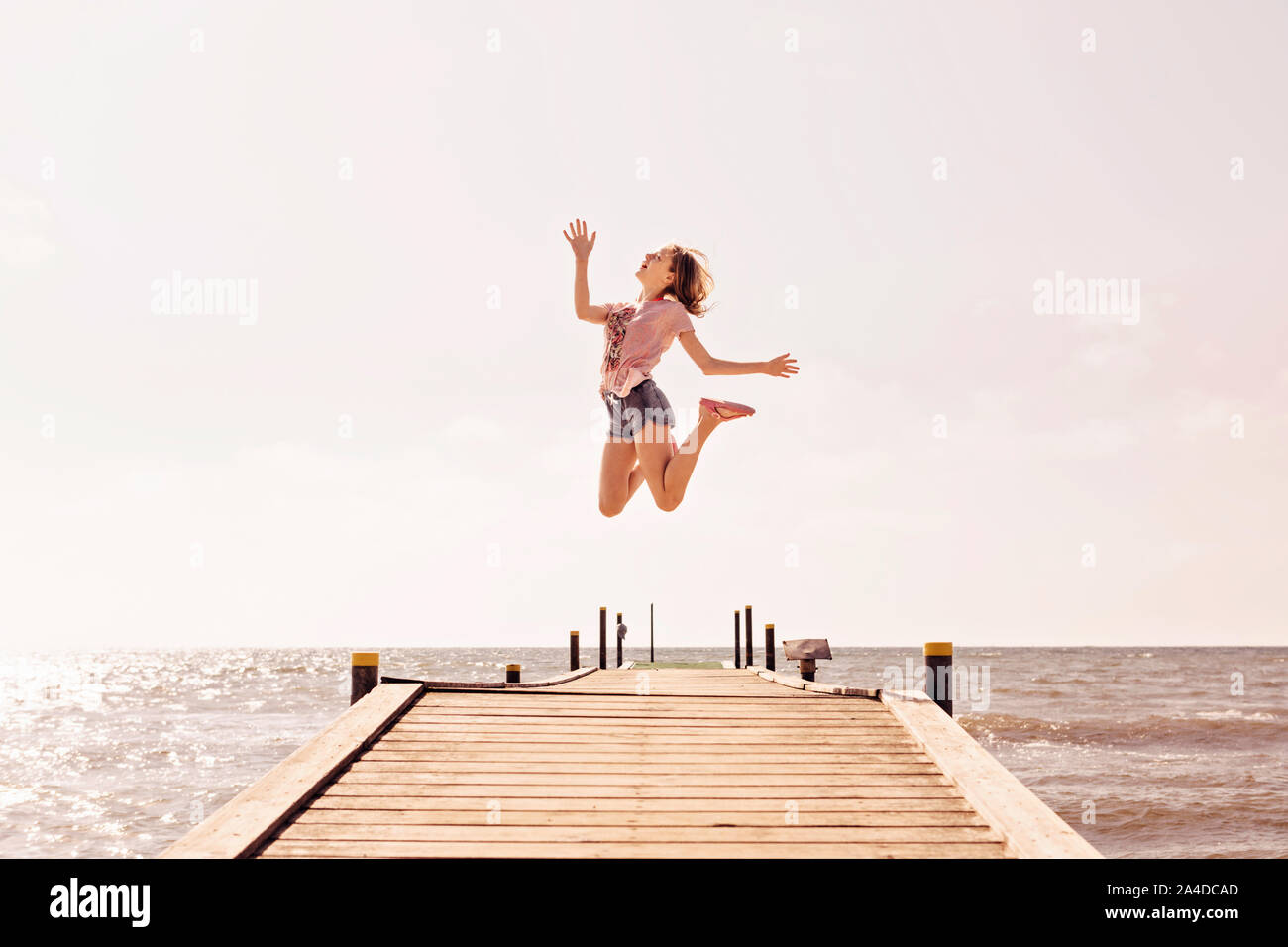 Girl jumping for joy on a pier by the sea, Denmark Stock Photo