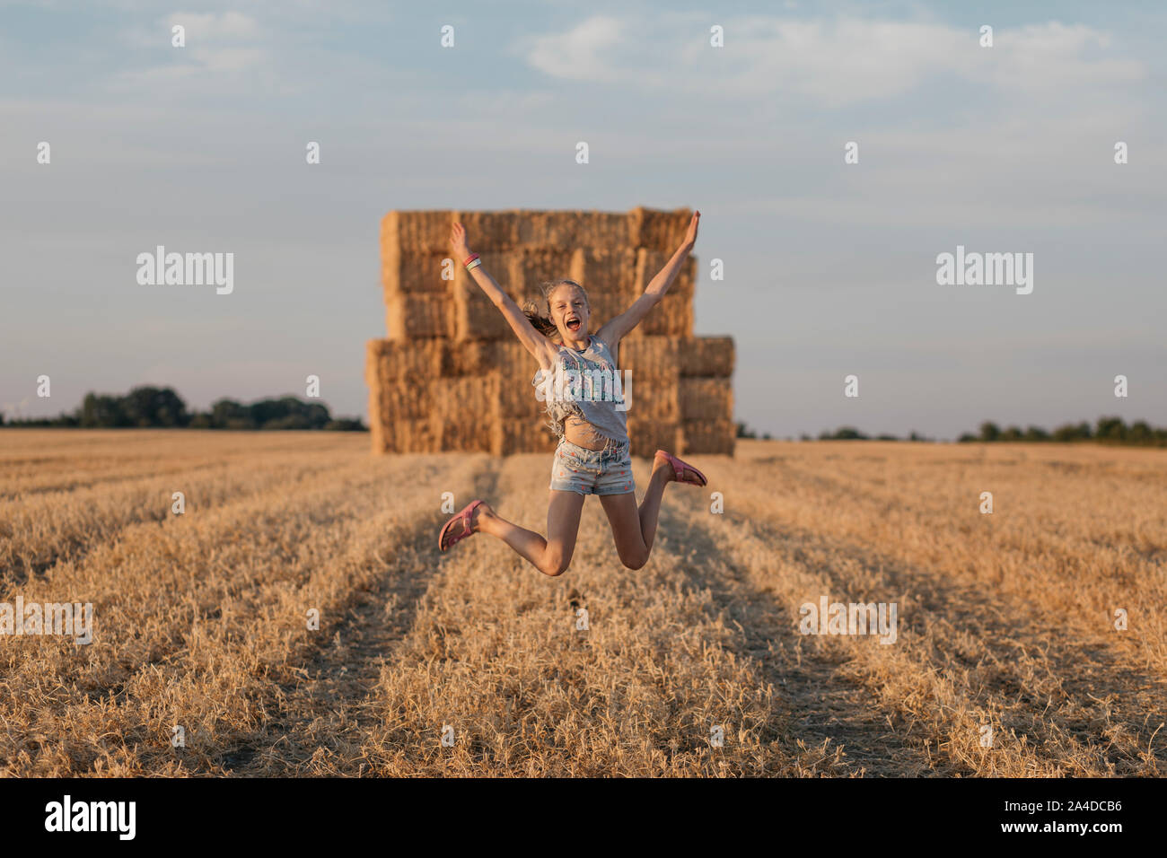 Girl jumping for joy in a field with hay bales, Denmark Stock Photo