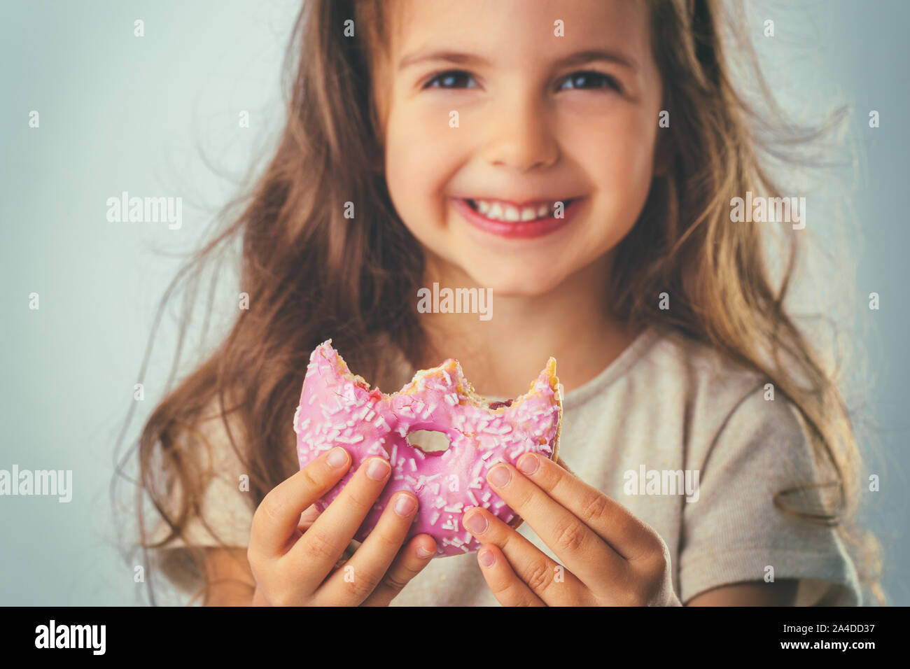 Sweet little girl eating pink donut. Stock Photo