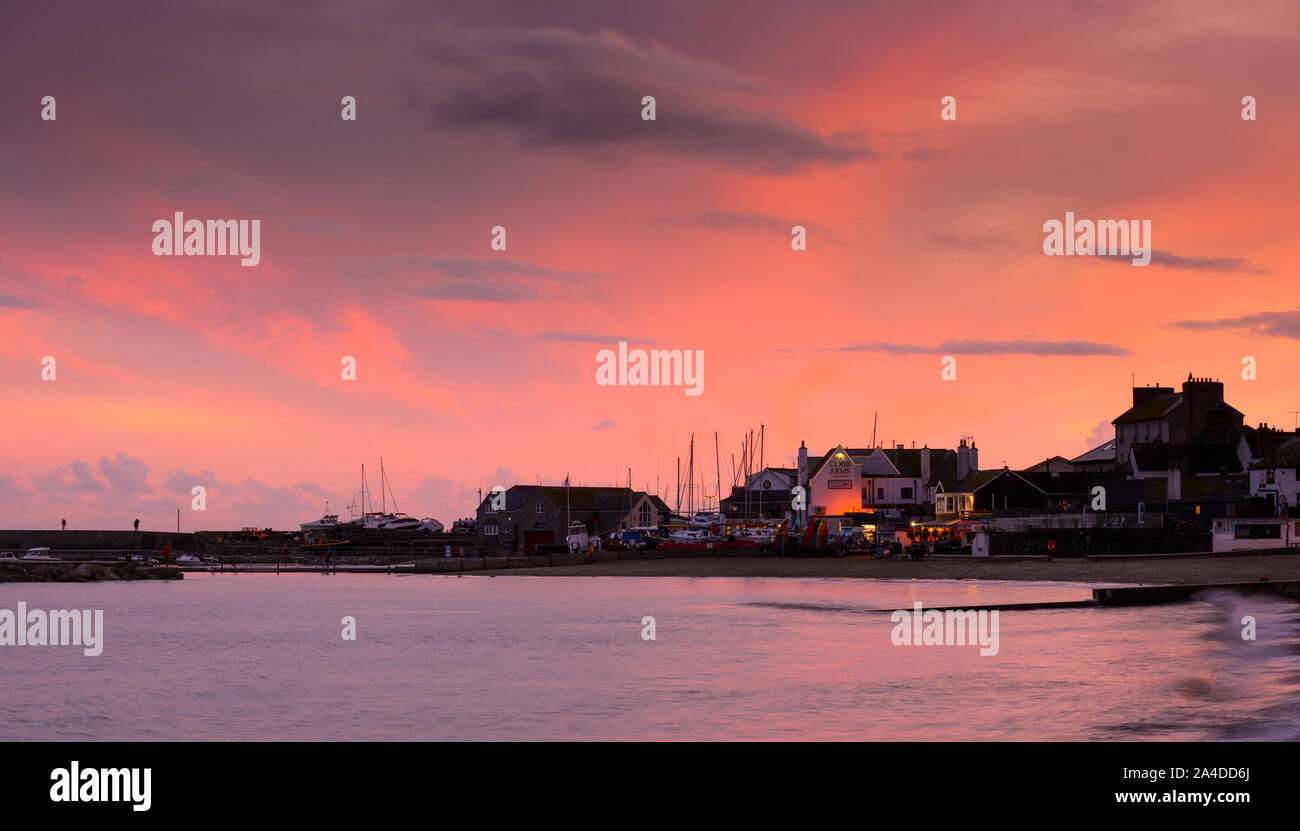 Lyme Regis, Dorset, UK. 13th October 2019. UK Weather: The sky over the Cobb Harbout at Lyme Regis glows with glorious pinks and reds at sunset after a dull and rainy day. Credit: Celia McMahon/Alamy Live News. Stock Photo