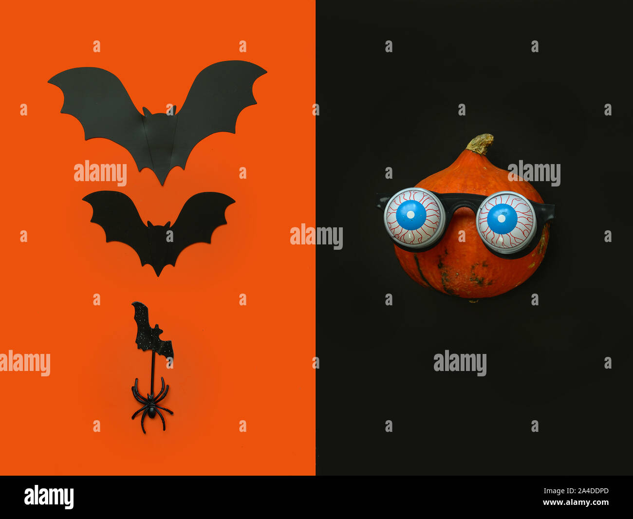 Flat lay Halloween background with pumpkin in in glasses horror symbol eyeball, spider and bats on black backdrop. Festive concept. Stock Photo