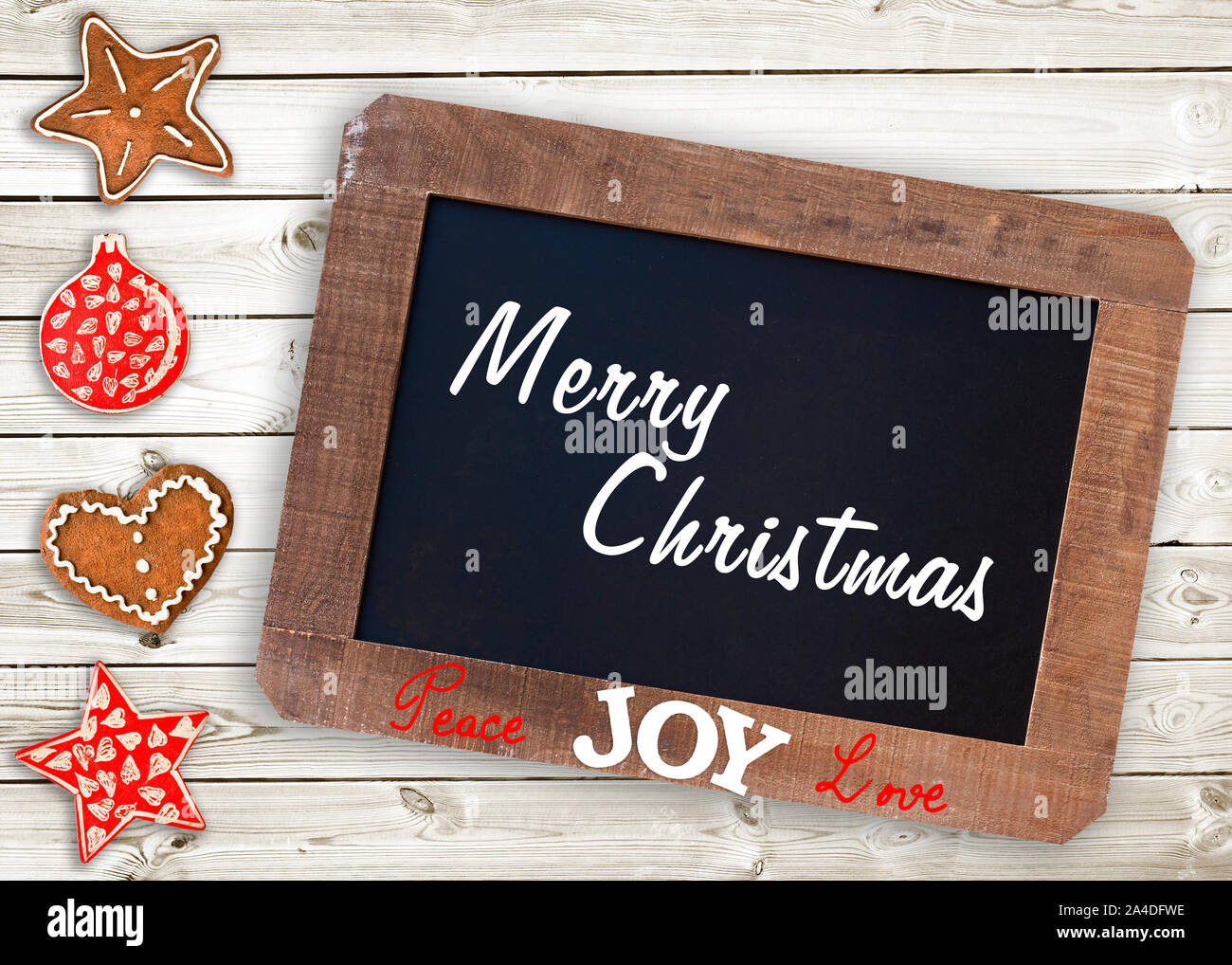 Merry christmas written on a vintage wooden chalkboard. Ginger bread cookies and Christmas ornaments on wooden planks. Christmas card. Stock Photo