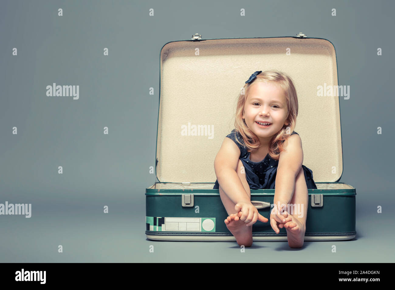 portrait of a 3 year old caucasian blond girl sitting in a vintage suitcase. studio shot Stock Photo