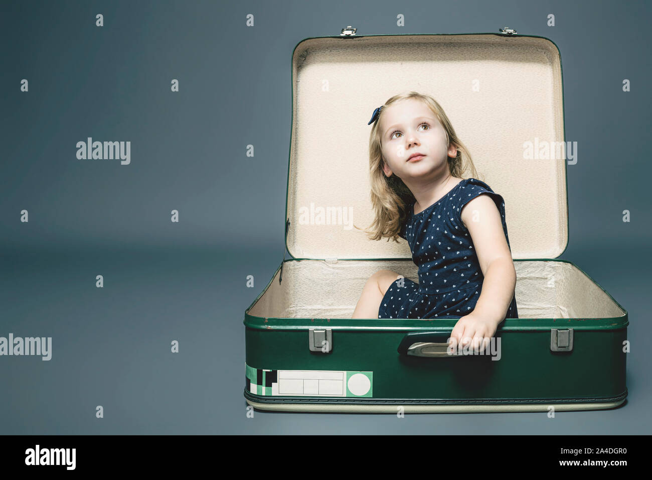 portrait of a 3 year old caucasian blond girl sitting in a vintage suitcase. studio shot Stock Photo