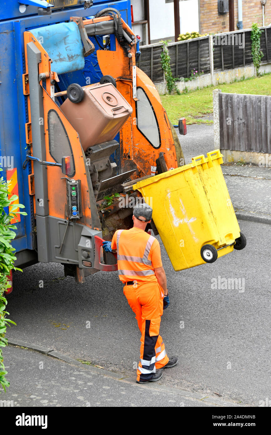 Refuse collection wearing high vis clothes operates lifting up controls back of dustcart to empty wheelie bin full of green garden recycling waste UK Stock Photo