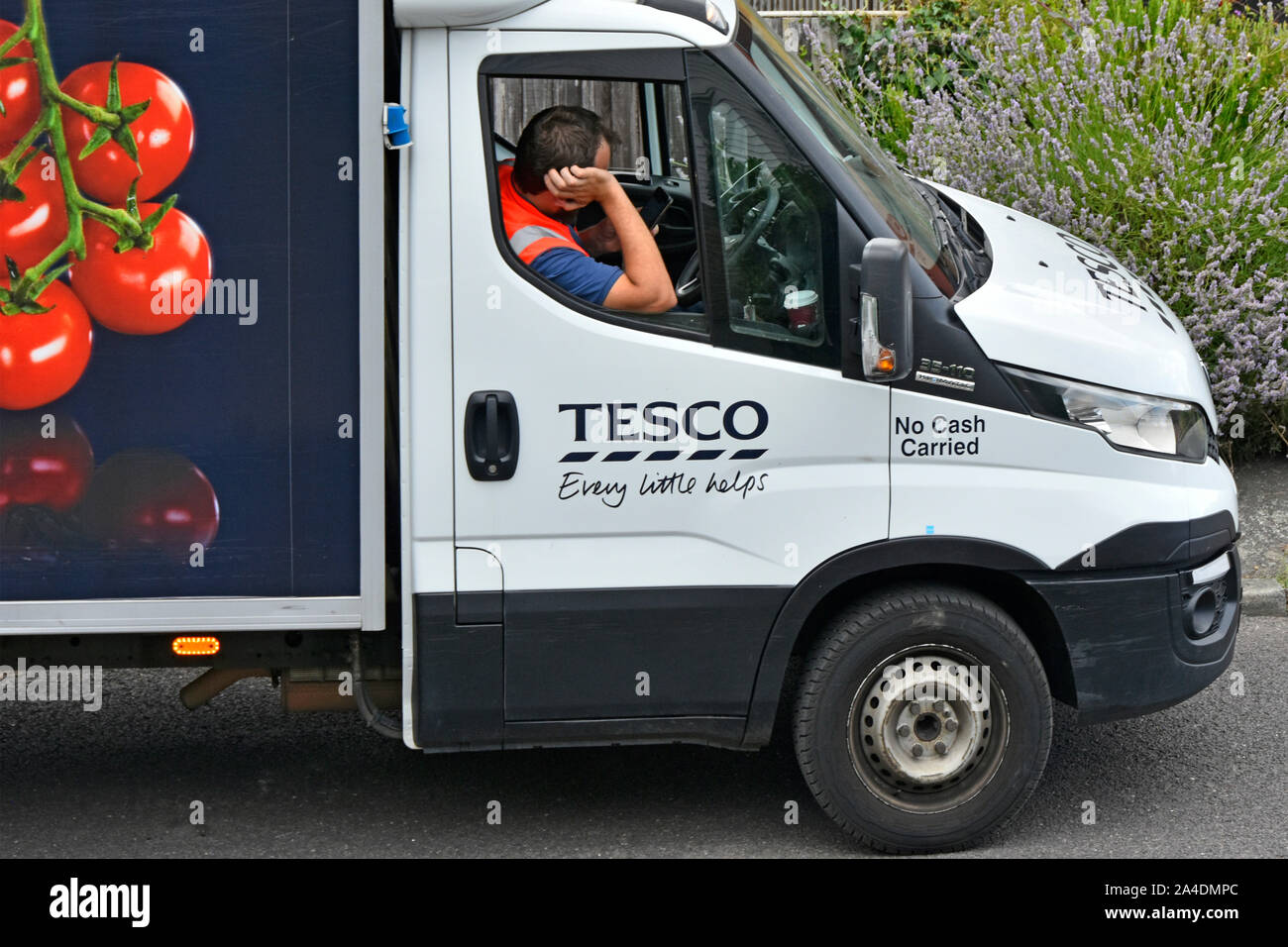 Street scene close up of Tesco supermarket home food supply chain delivery driver man arrives early &  waits in van for his customer Essex England UK Stock Photo