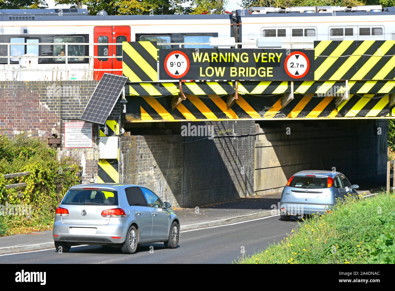 Close up of metric warning sign & black yellow hazard stripes painted on side of very low train railway bridge above cars driving into Ely England UK Stock Photo