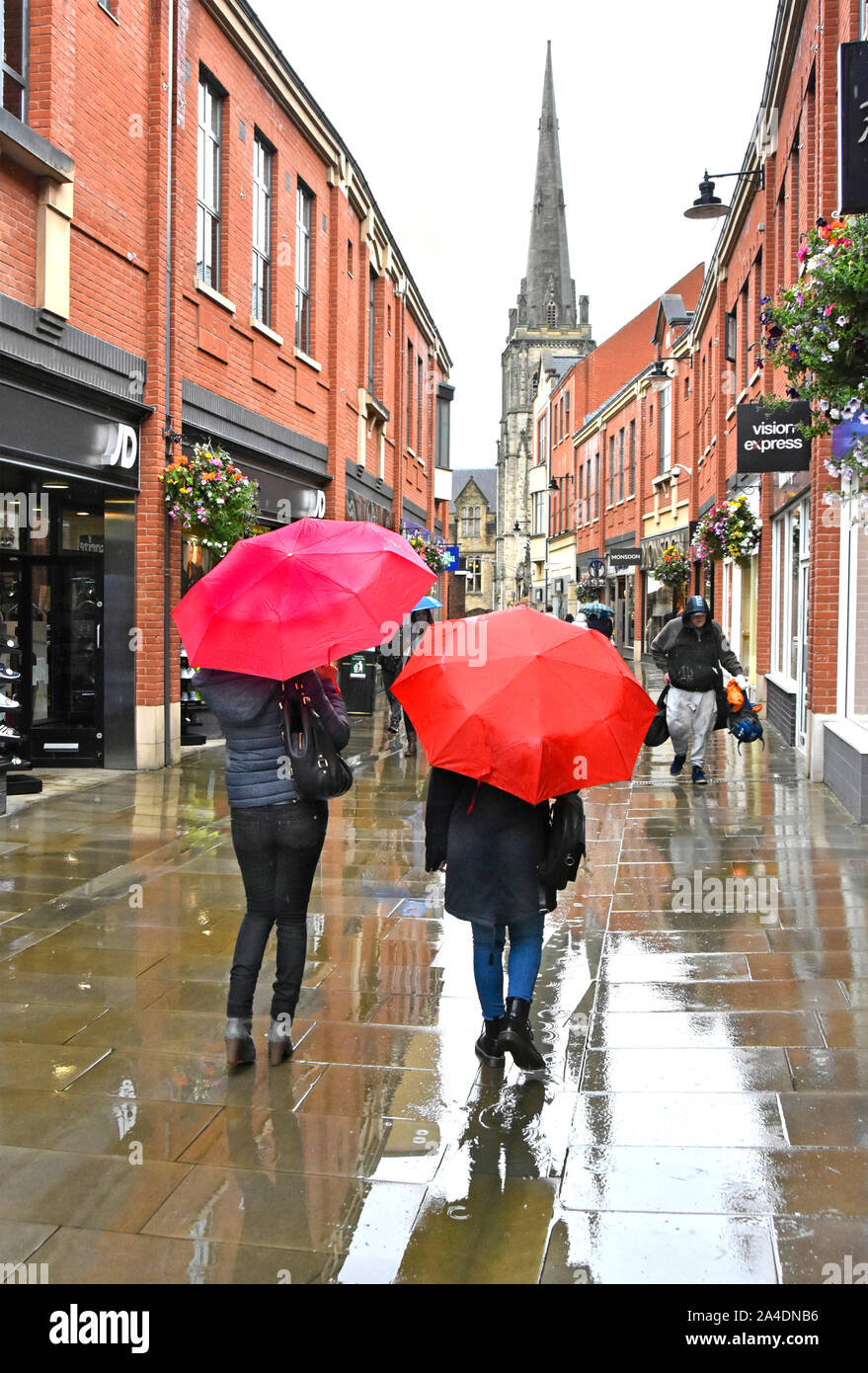 Raining on two women walking along wet weather town centre pedestrians only shoppers street zone in rain under red umbrella summer Durham England UK Stock Photo