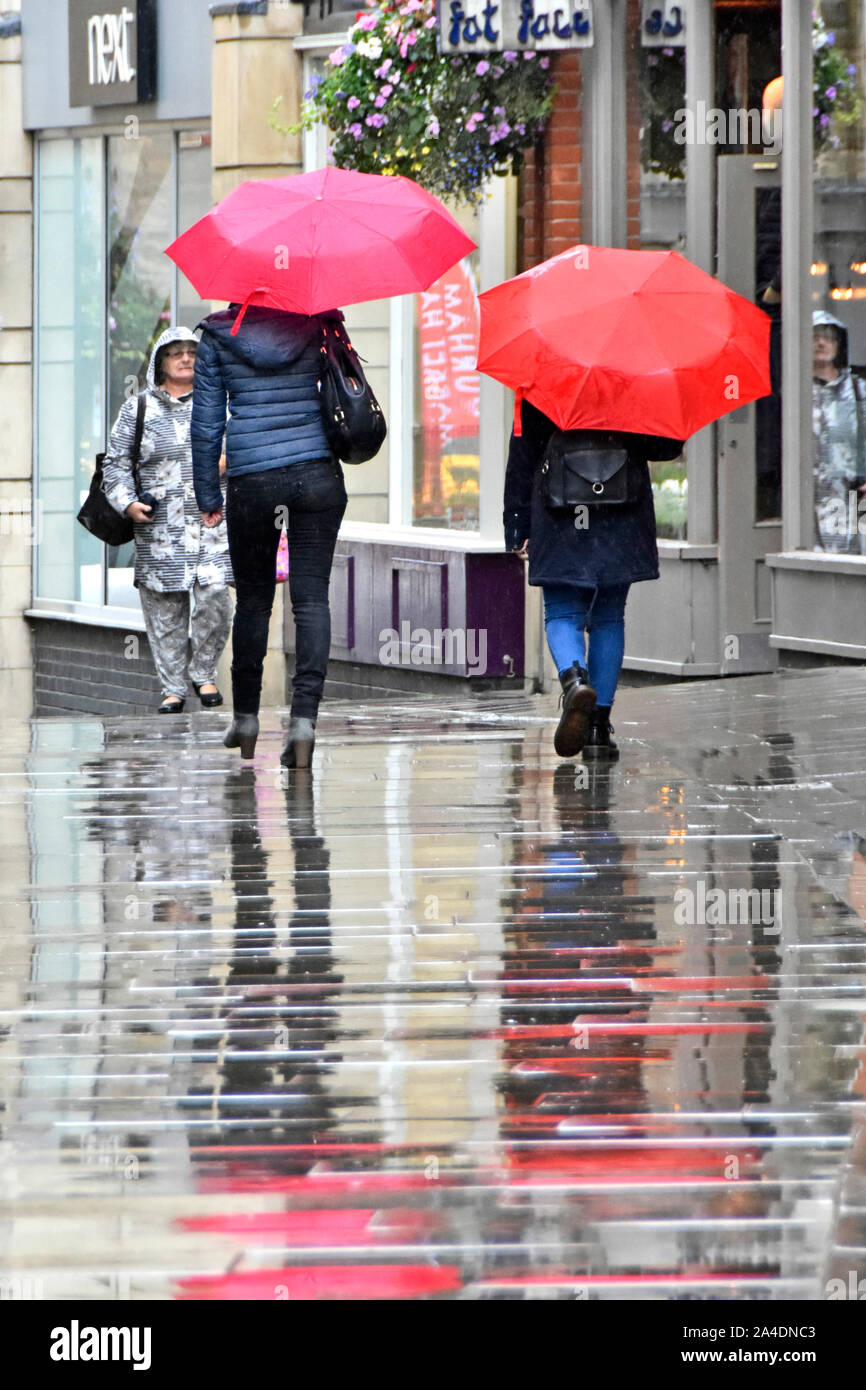 Raining two women walk in wet weather in town centre pedestrians only shoppers street zone in rain under red umbrella & reflections Durham England UK Stock Photo