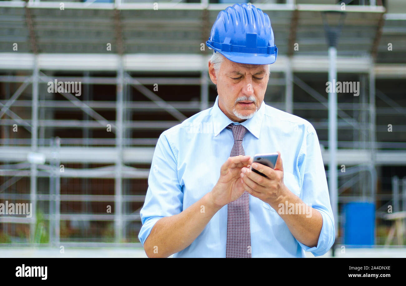 Senior engineer using his smartphone outdoor on a construction site Stock Photo