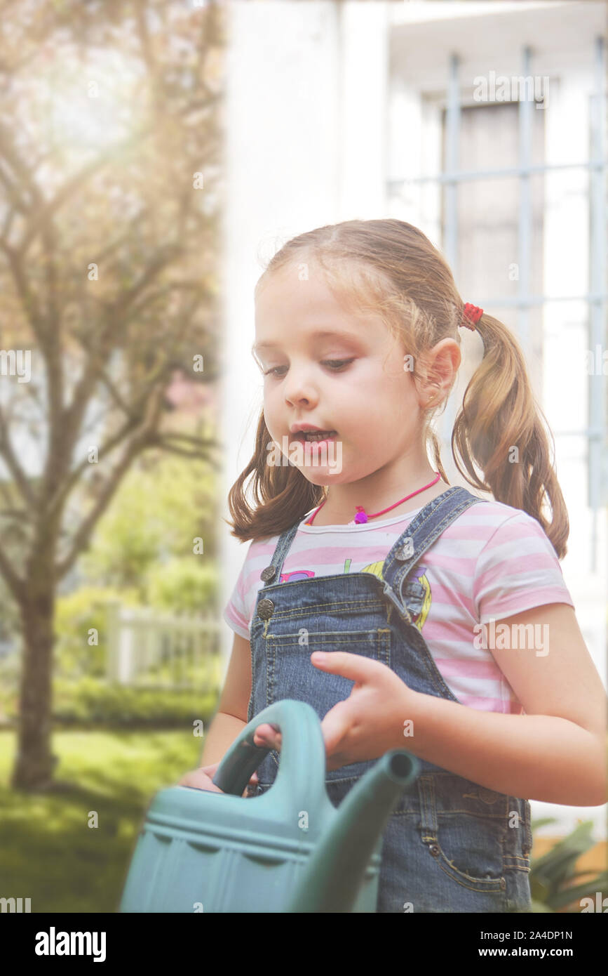 Little girl in a home garden with a watering can agains a sun flare at sunset. Empty copy space for Editor's text Stock Photo