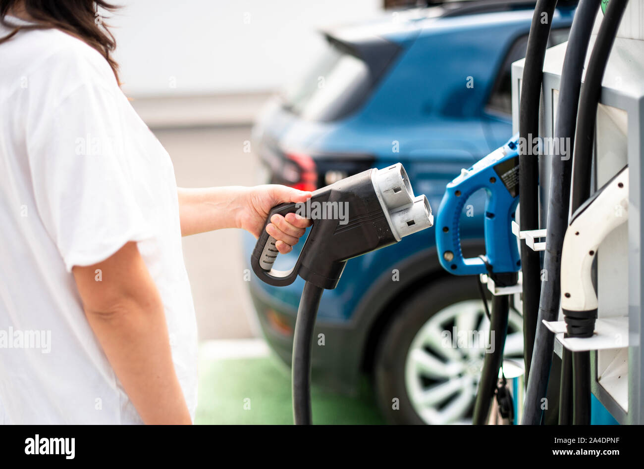 Woman charge her Electric car on gas station. Blue car and electric plug for charging. Ecology fuell concept. Stock Photo