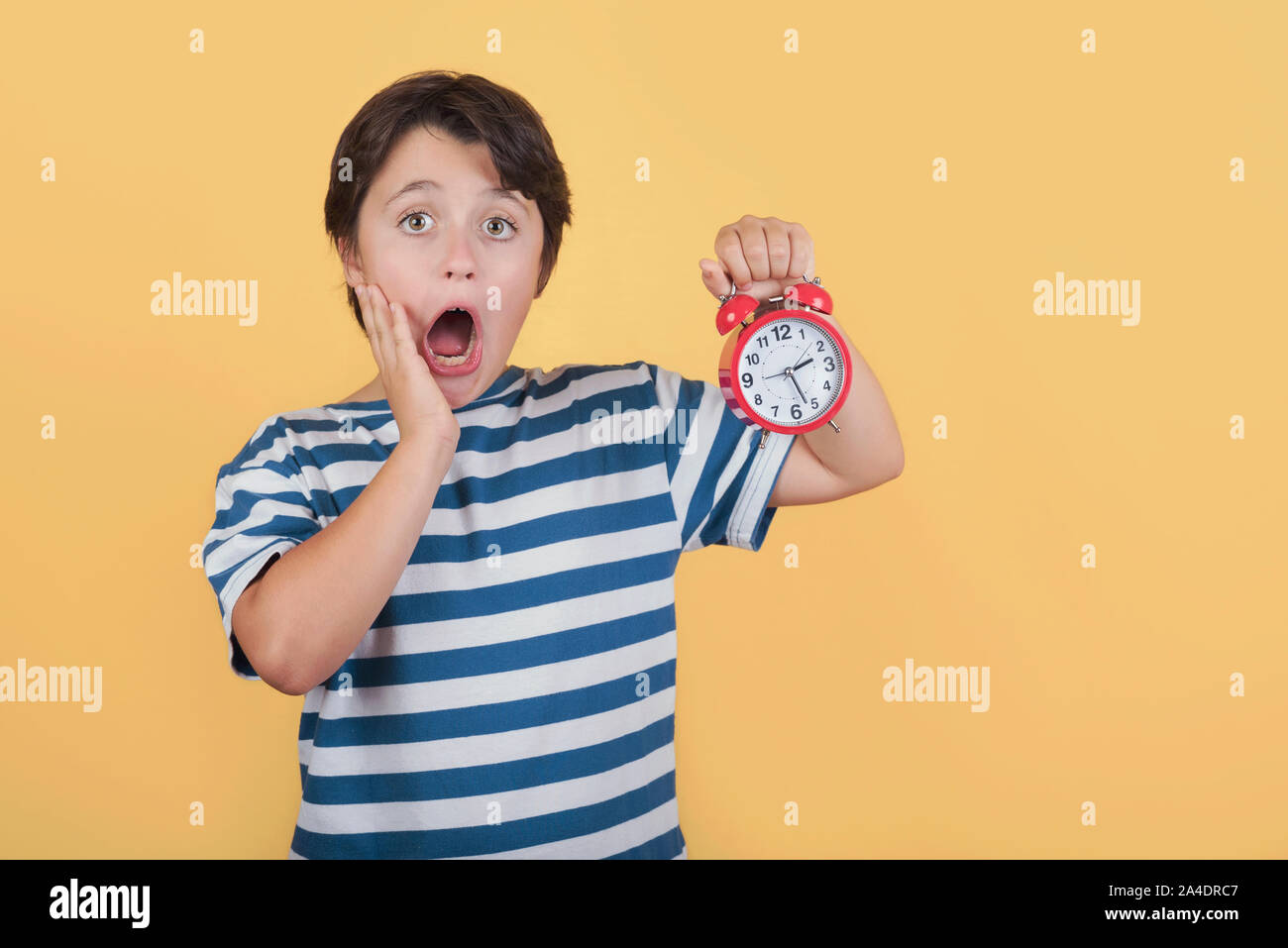 Shocked child holding alarm clock on yellow background Stock Photo