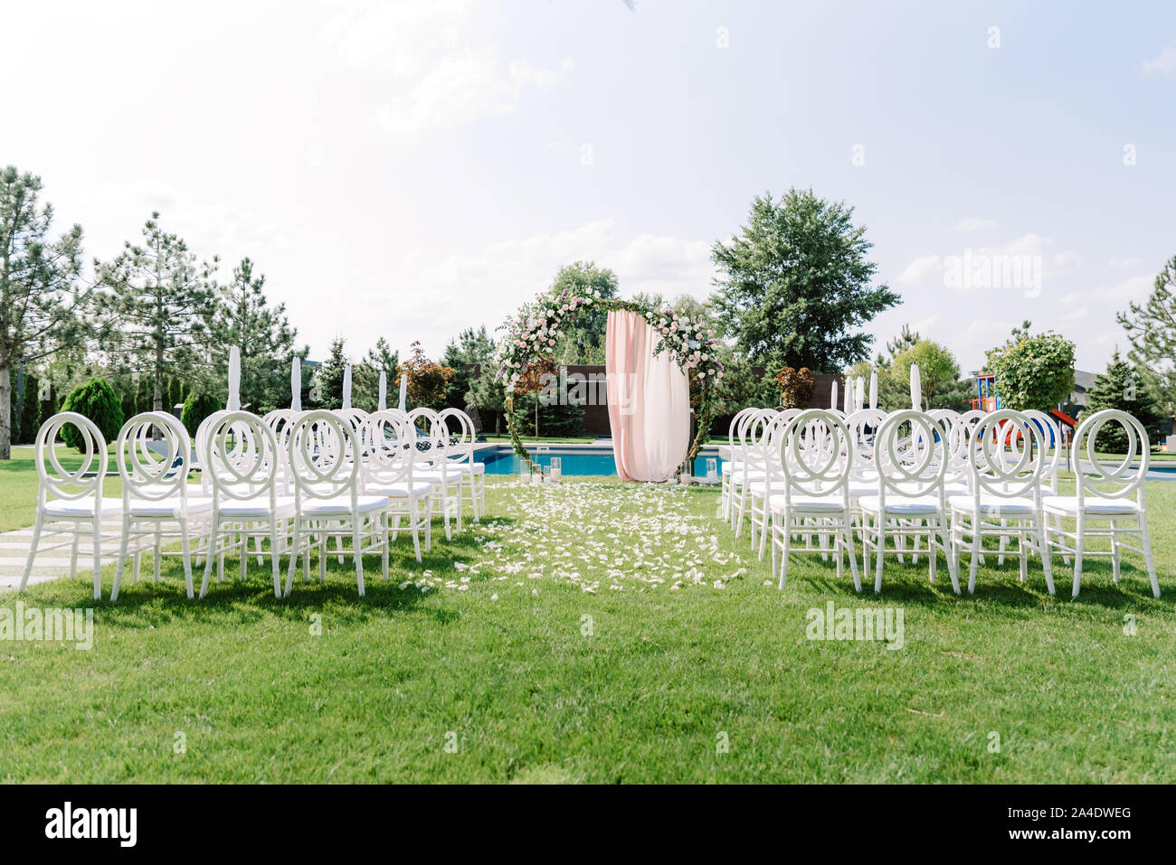 Wedding round arch and transparent chairs made of plastic for guests on the green lawn near the basein Stock Photo