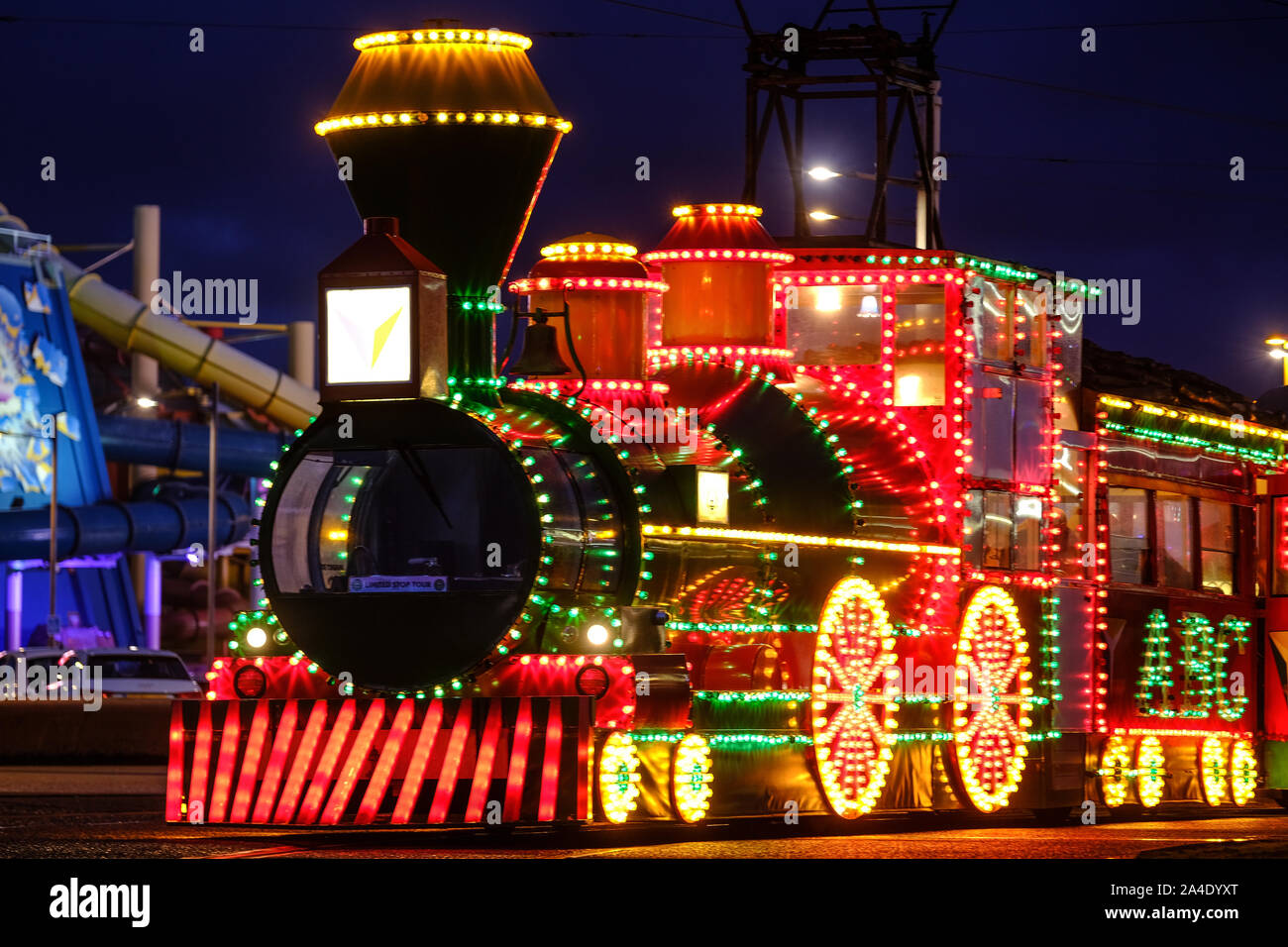 An illuminated Blackpool Tram by The Water Park attraction on the Promenade Stock Photo