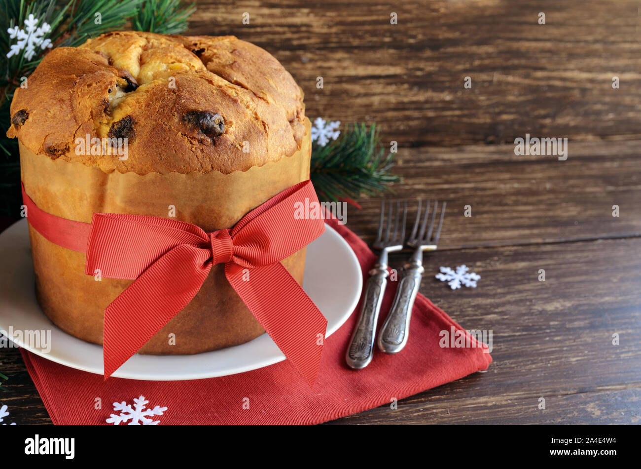 Traditional Panettone cake with dried fruits on the wooden table with  Christmas decoration. Italian sweet bread with red ribbon and bow for celebrate Stock Photo