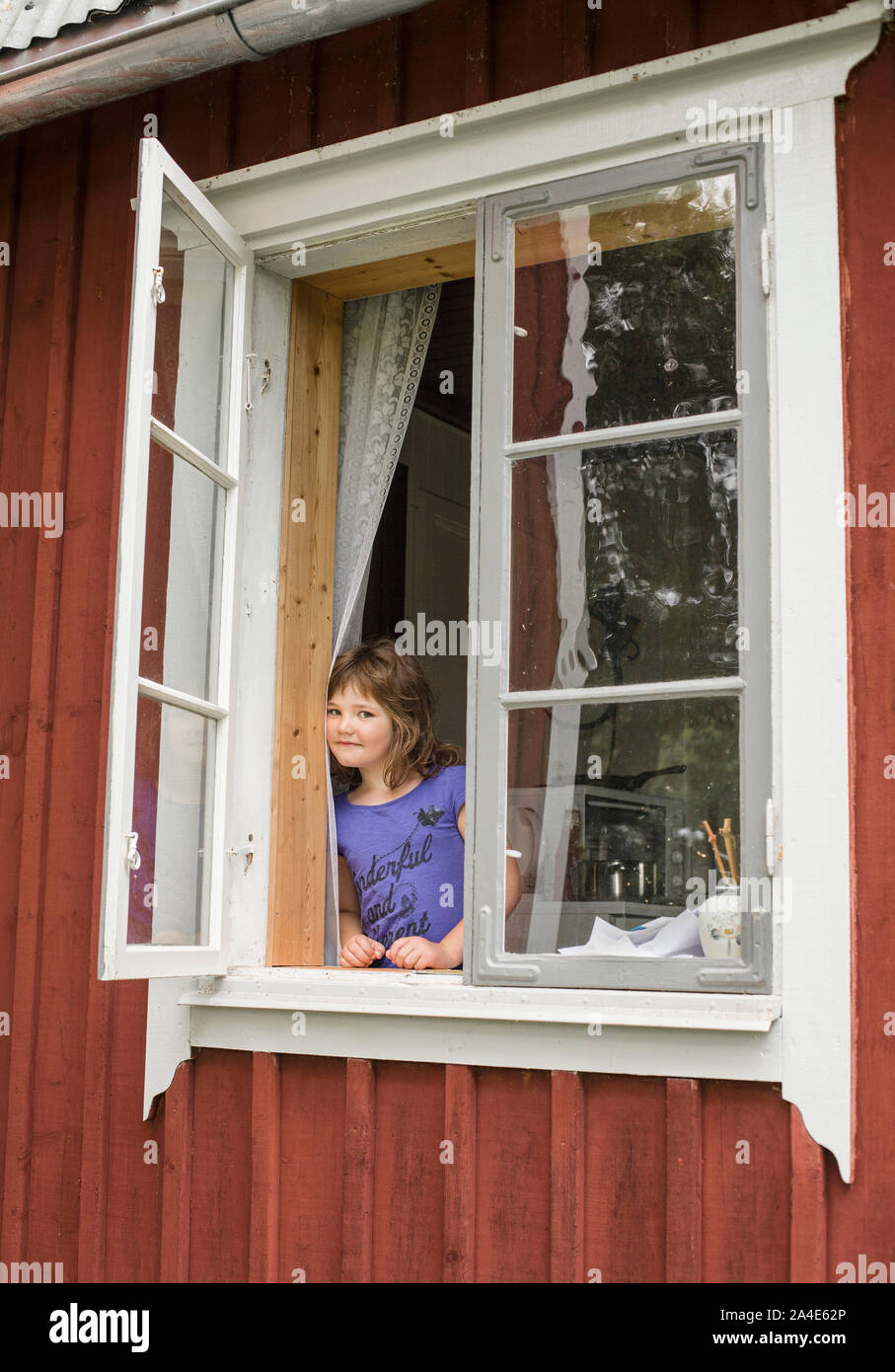 Young girl in an open window on a countryside cottage, Sweden. Stock Photo