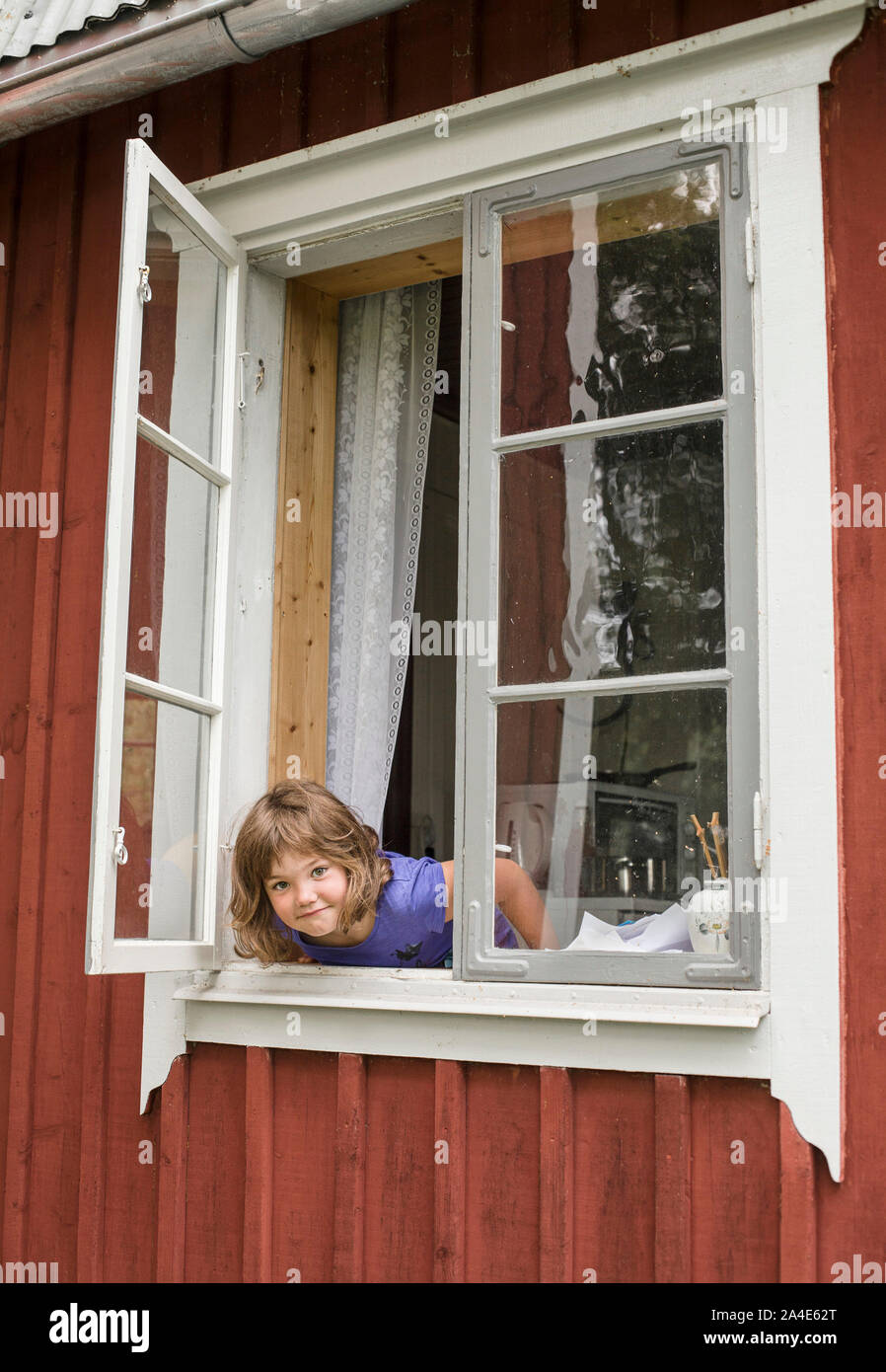 Young girl in an open window on a countryside cottage, Sweden. Stock Photo