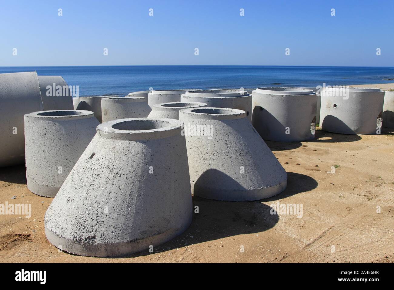 Large new concrete circular pipes lying down on a sandy beach for the construction of sewerage system background view of clear blue sea and sky Stock Photo