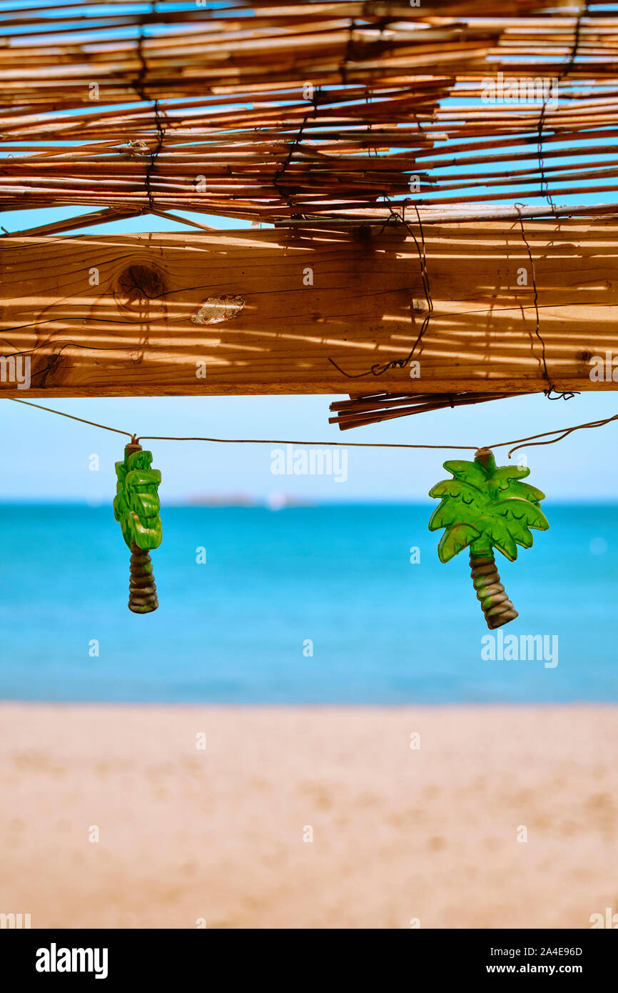 Palm tree shaped string lights decorating a rustic beach bar cafe with blue sea and sky beach background - tropical summer beach holiday paradise Stock Photo