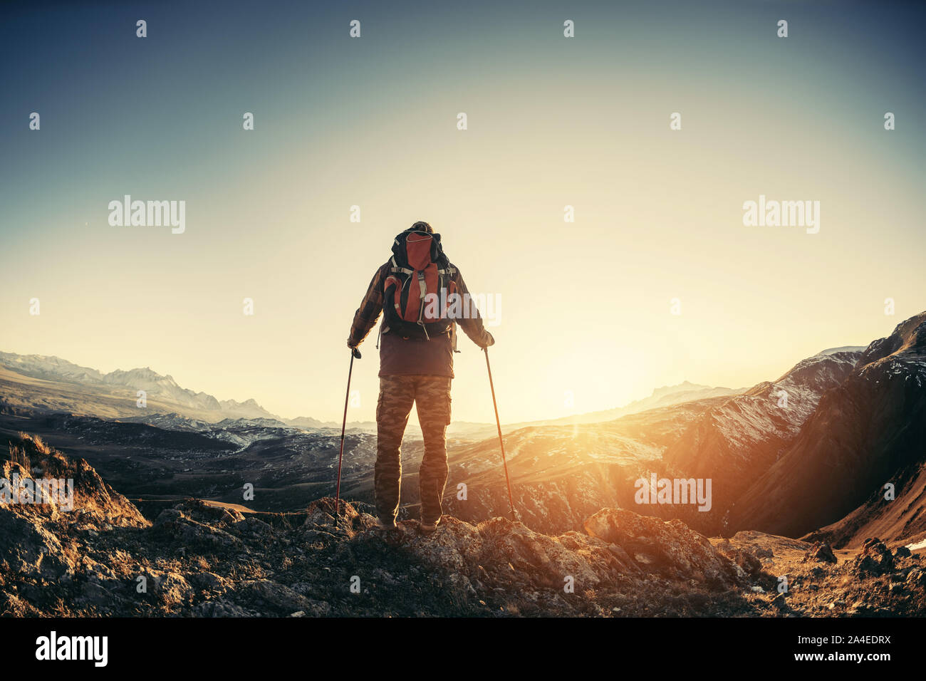 Hiker with backpack and walking poles stands against mountains Stock Photo