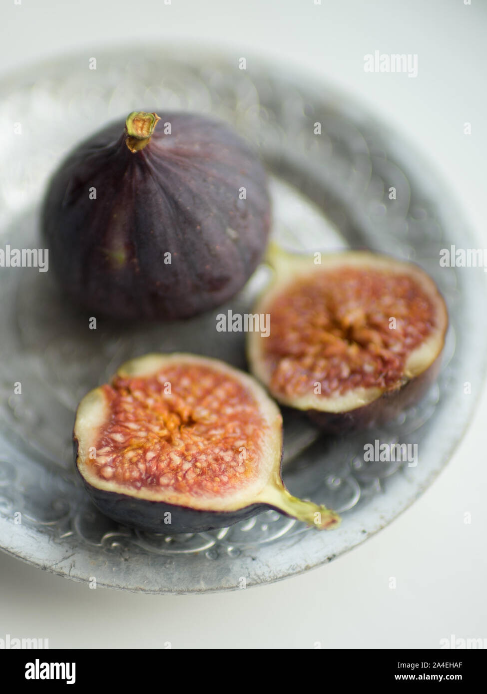 Two ripe figs. One whole fig and the second cut in half on a white table. Stock Photo