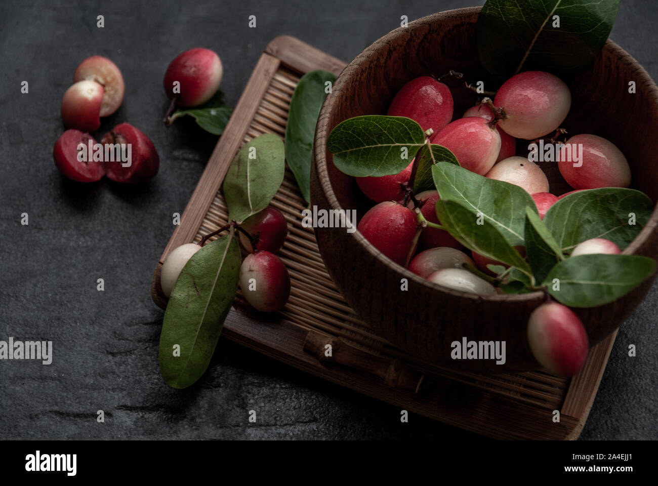 Bengal-Currants, Carandas-plum or Karonda fruit (Carissa carandas L.) sour taste fruit in Wooden cup on wicker. Oblique view from the top. Stock Photo