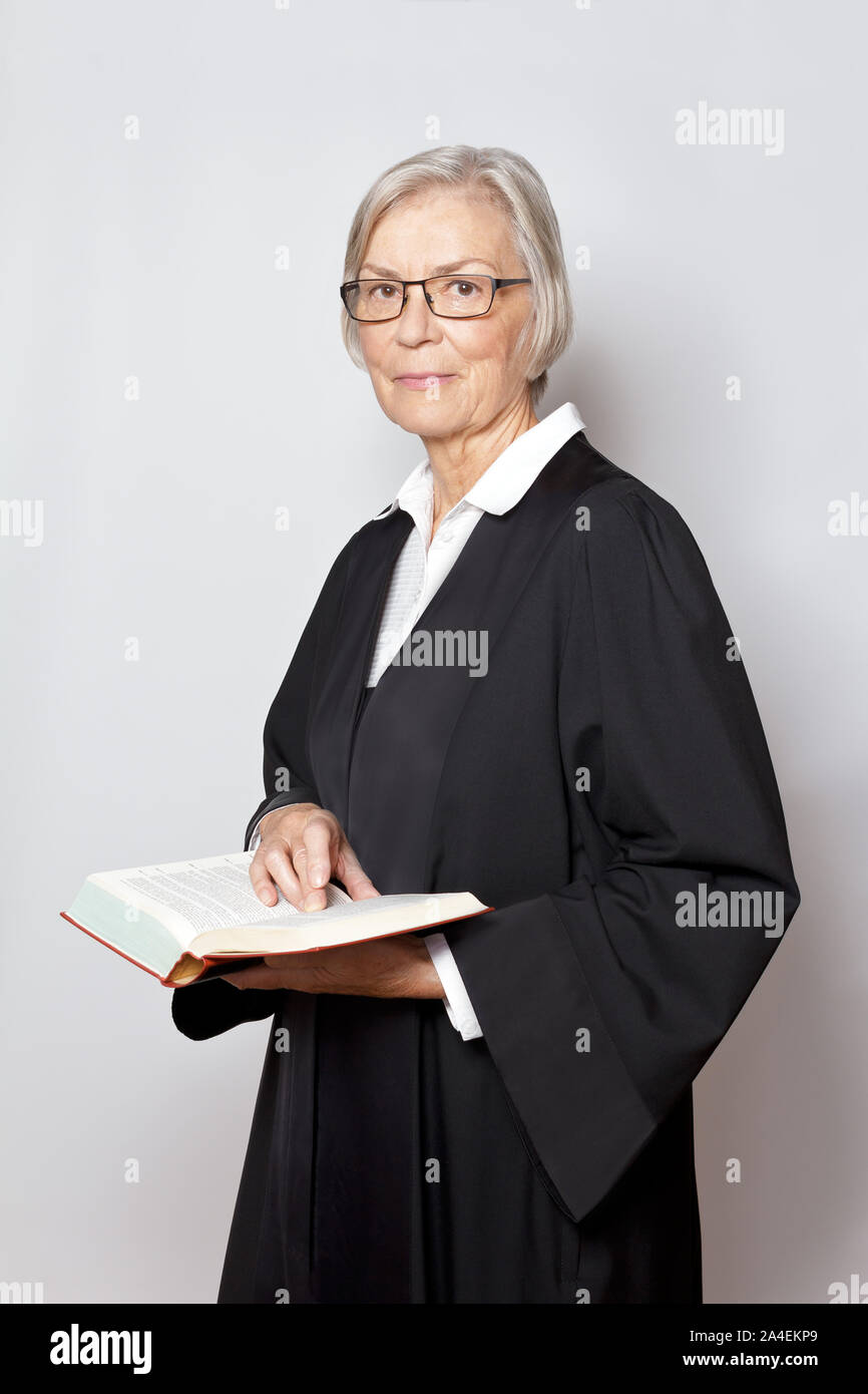 Female lawyer concept: portrait of an elderly woman in a black gown holding a legislative text book. Stock Photo