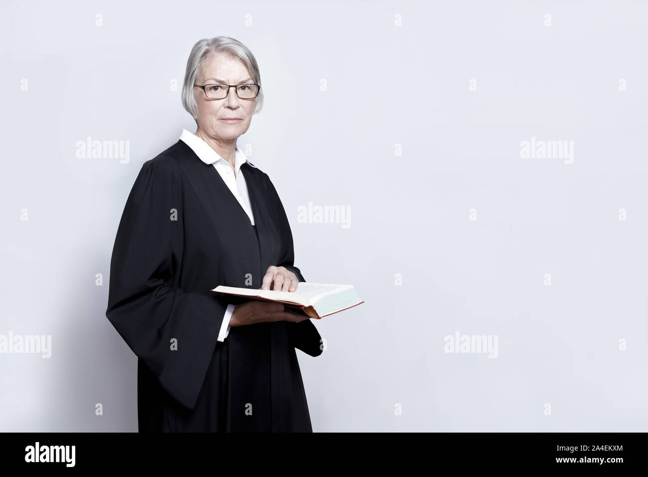 Female lawyer concept: mature woman in a black gown holding a legislative text book, copy space. Stock Photo