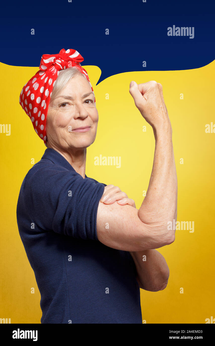 Defy age concept: mature woman with clenched fist rolling up her sleeve, background template, copy space Stock Photo