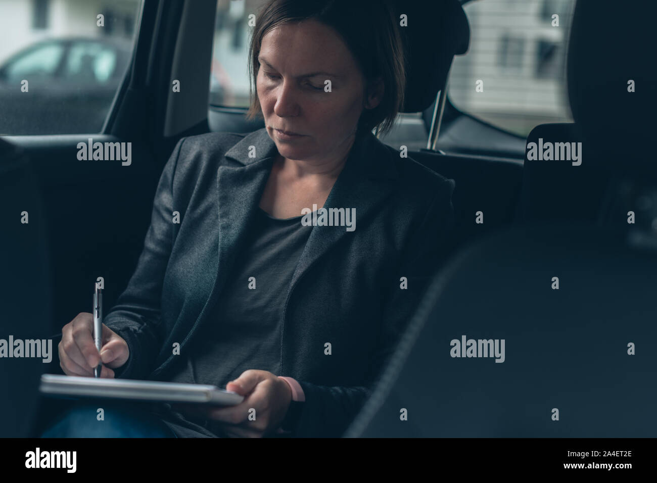 Businesswoman doing paperwork and analyzing business report while sitting in car at the back seat Stock Photo